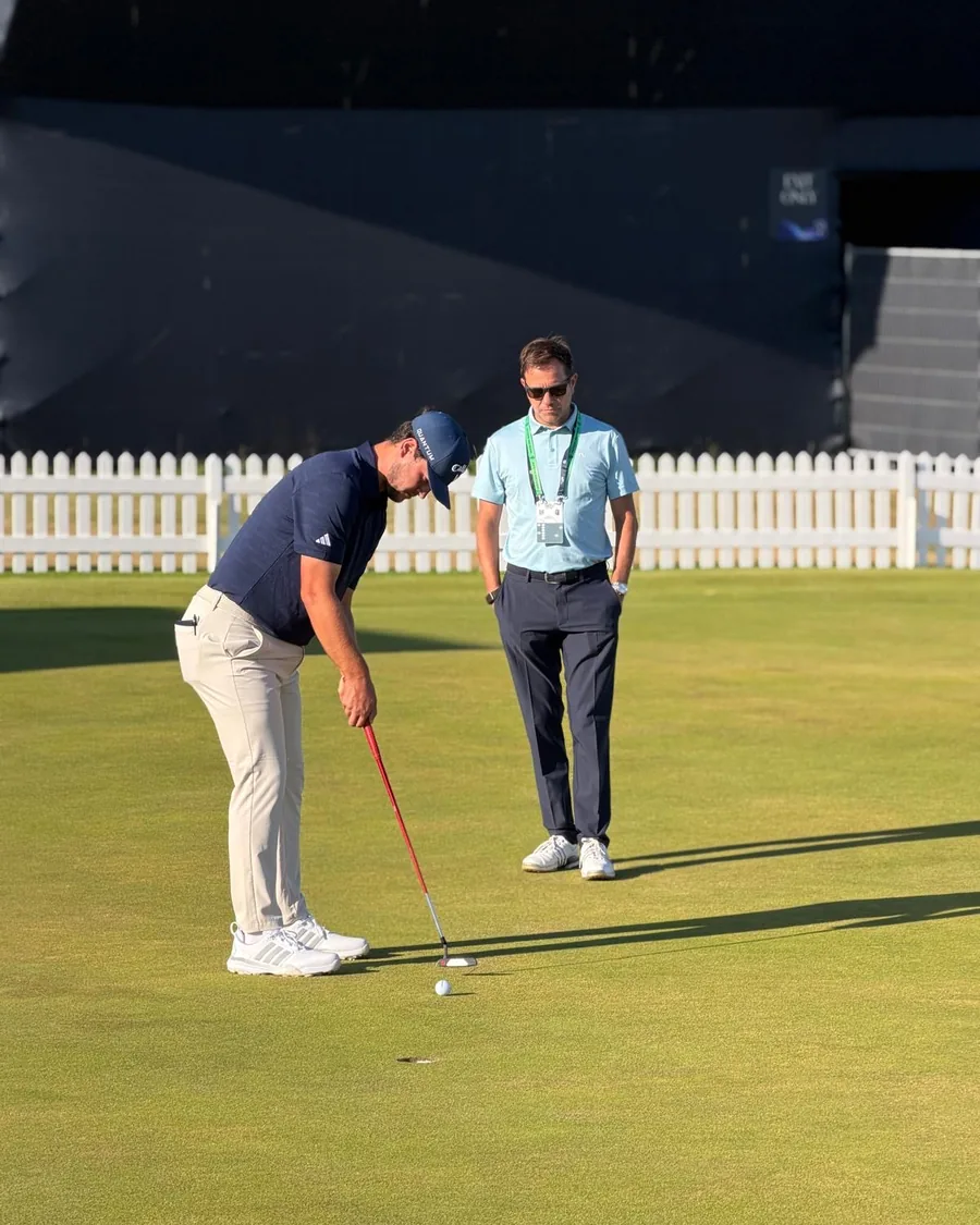 A coach standing over a player lining up a putt on a links green in evening light.