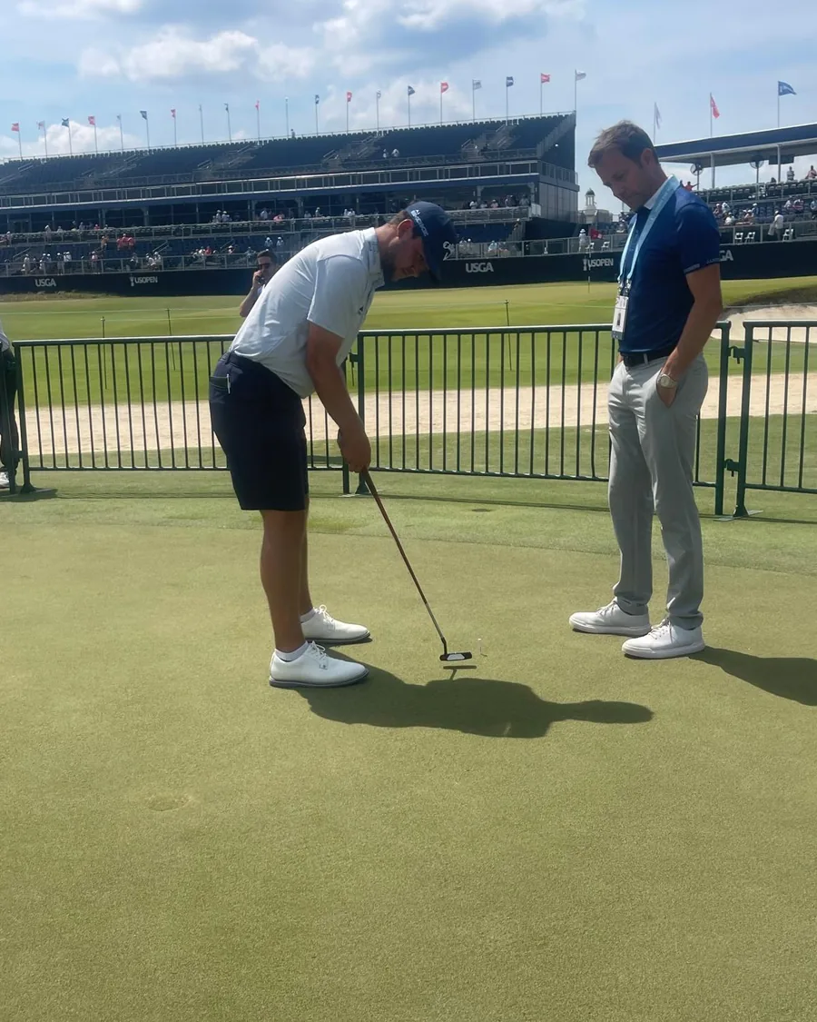 A coach watching closely as a player strokes a putt on a championship practice green.